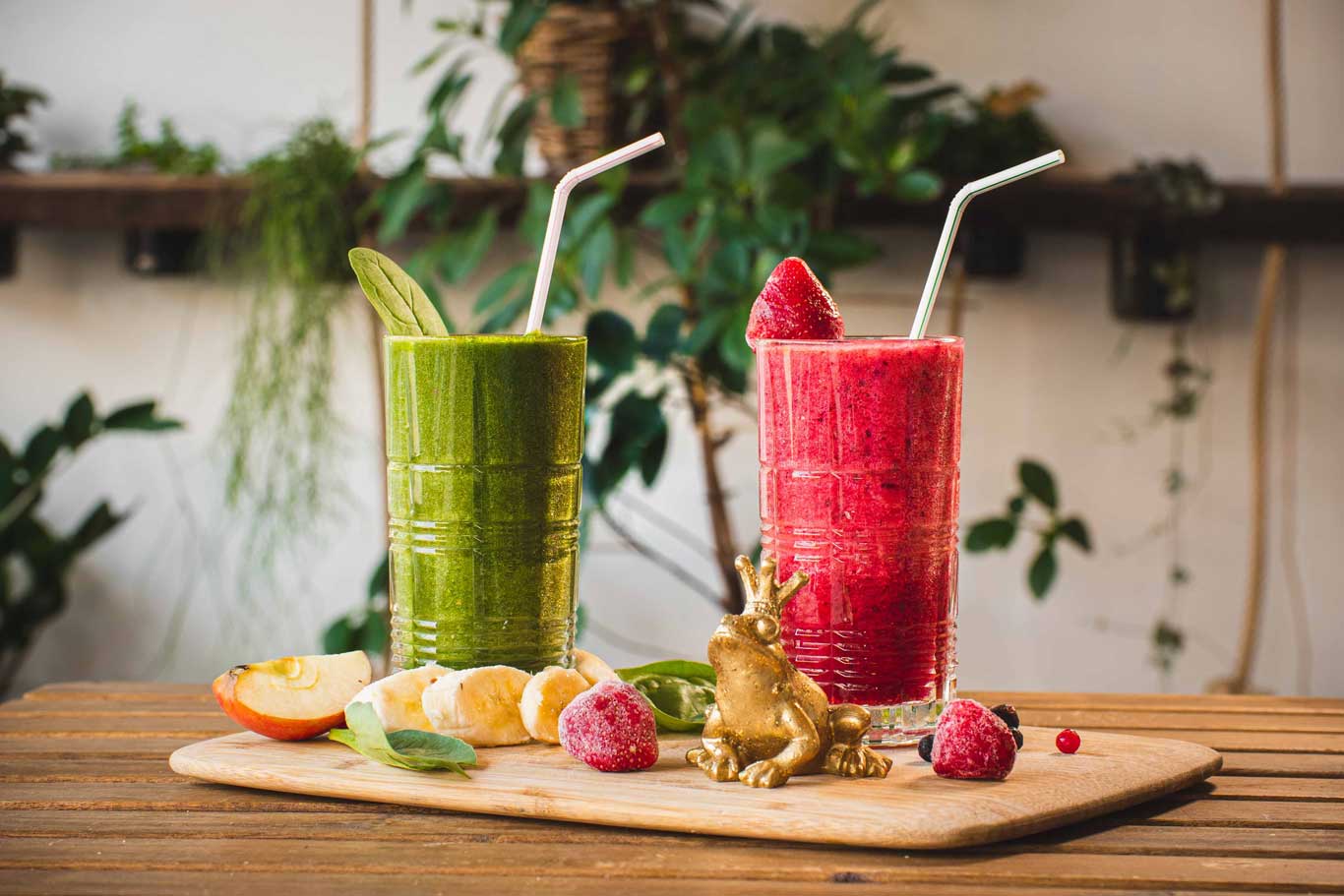 Zwei Gläser Smoothies, ein grüner und ein roter, serviert mit Früchten.